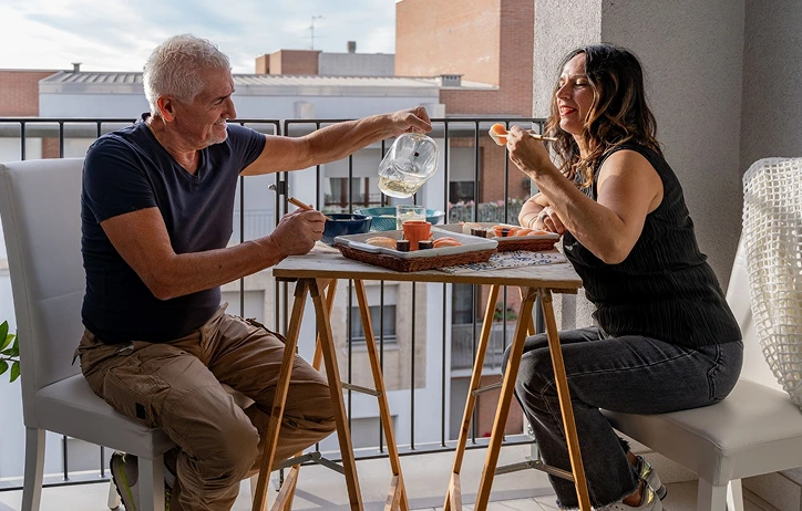 Man and woman eating breakfast on balcony.